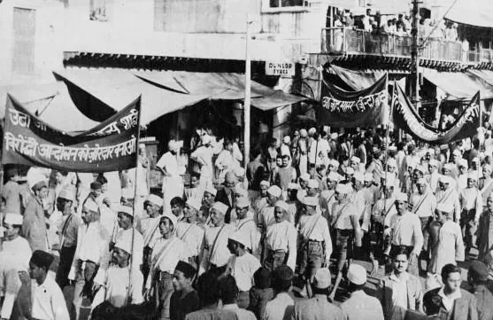 A street procession of Indian National Congress supporters in white caps carrying banners through a crowded market street, New Delhi, 1937
